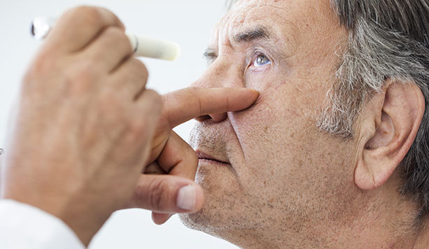 An elderly man's eye being checked with a pen light<br />

