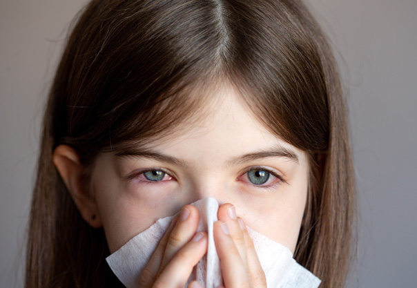 Young girl blowing nose suffering from allergies