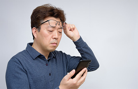 Man lifiting up his glasses and having trouble seeing his cell phone
